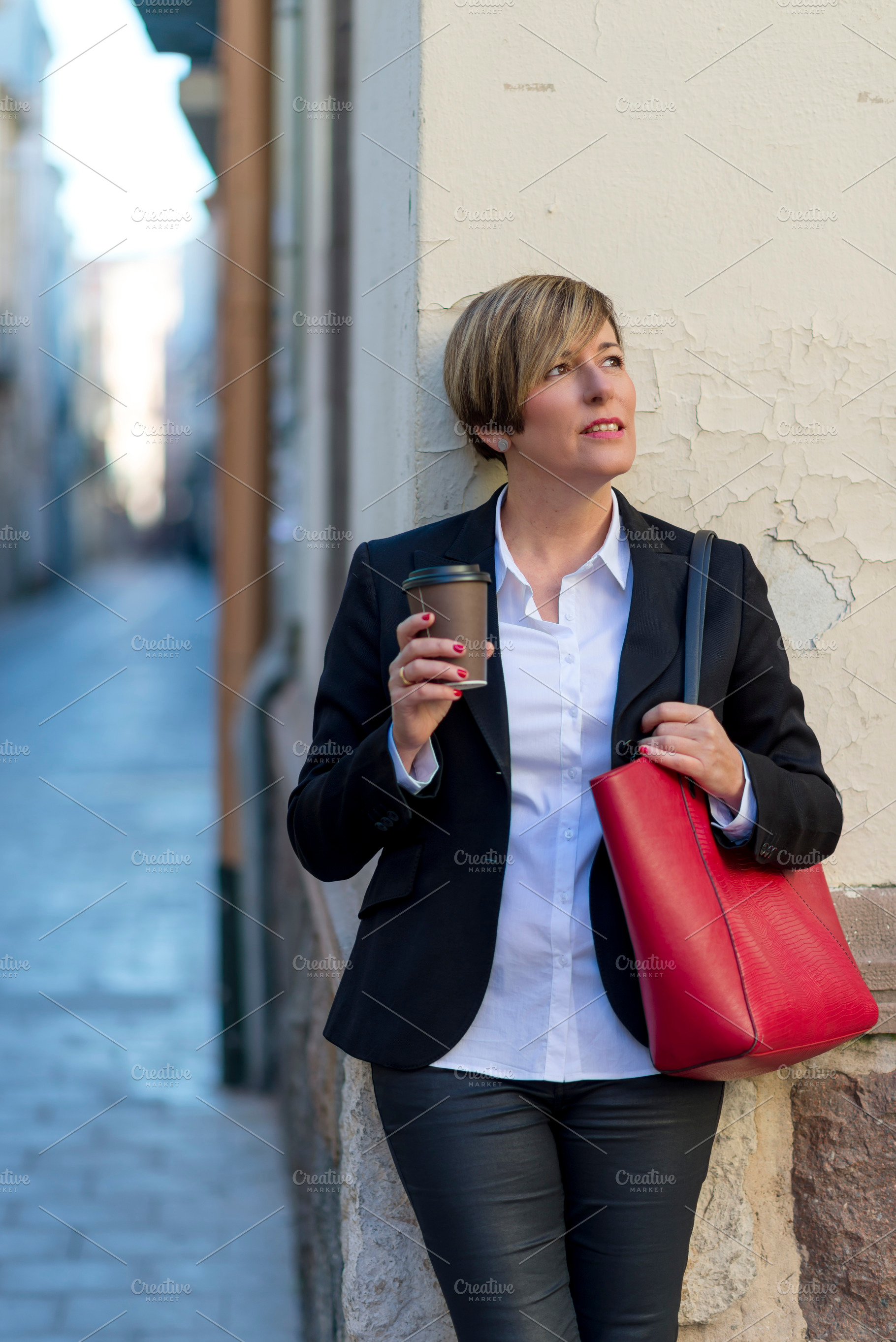 Businesswoman with coffee standing in city street, a Photo by RF Images