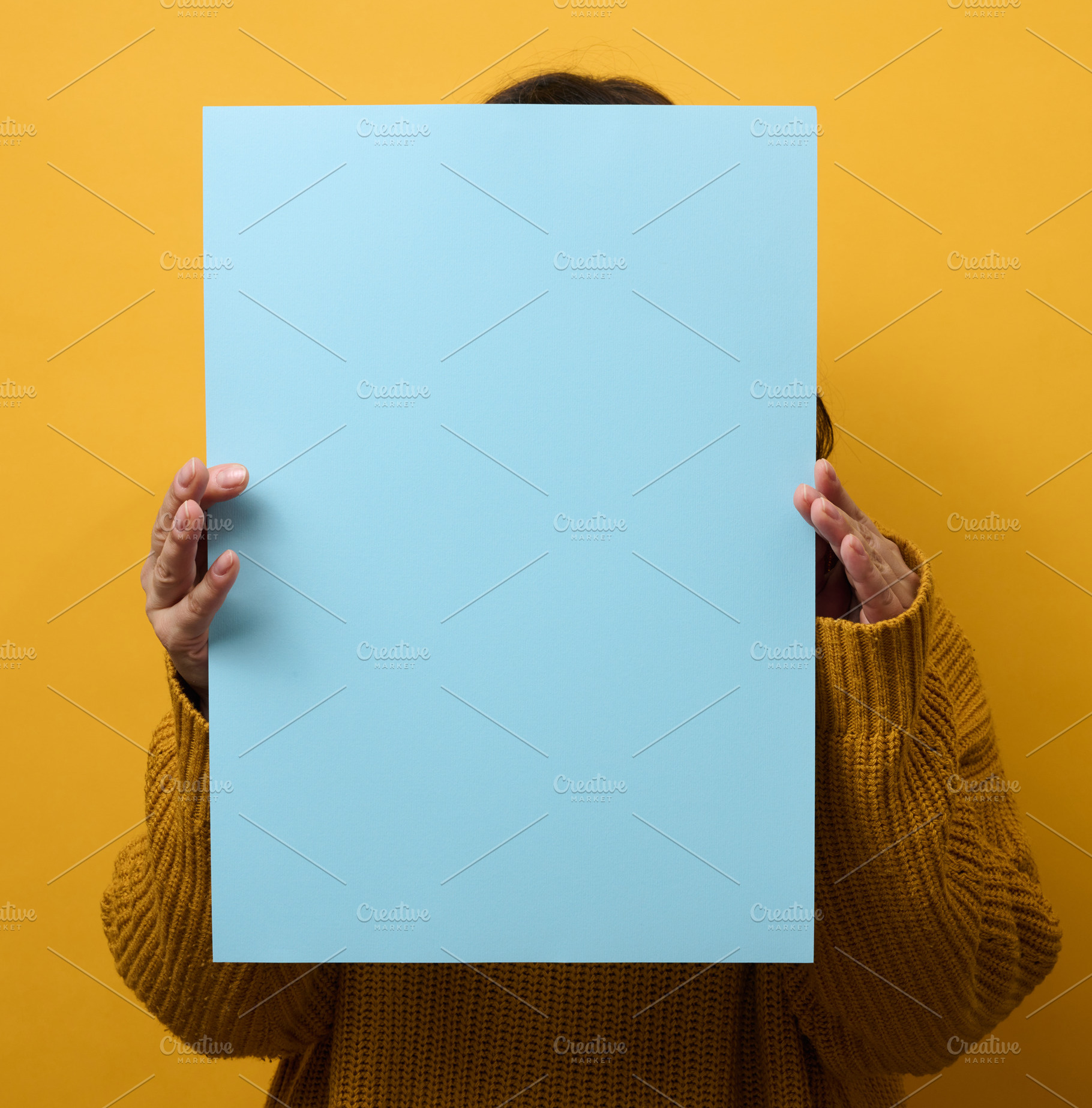 woman in an orange sweater holds a blank sheet of paper on a yel, a Person Photo by ndanko