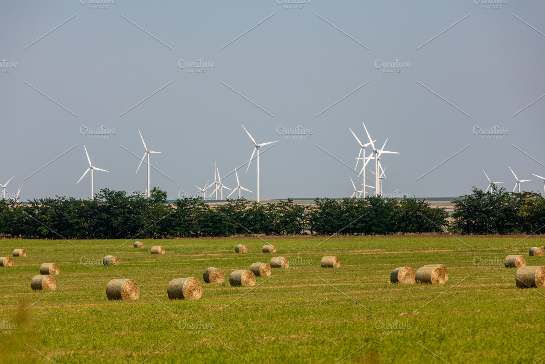 Modern wind turbines overlook a green field scattered with round hay bales unde, a Nature Photo by Ales Munt