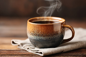 Warm cup of coffee resting on a cloth with steam rising in a cozy indoor settin, a Food & Drink Photo by AlyaAnd