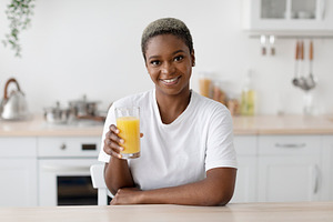 Smiling millennial african american woman in white t-shirt hold glass of organi, a Person Photo by Prostock-Studio