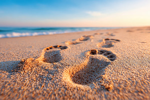 Footprints in sand on a beach at sunrise, a Background Photo by AlyaAnd