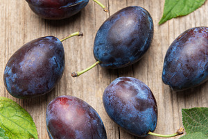 Ripe purple plums fallen on wooden table, a Food & Drink Photo by Olena Rudo