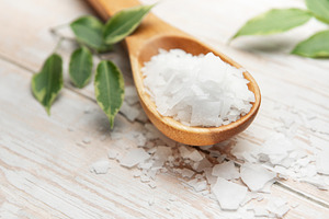 Magnesium chloride flakes on wooden spoon with green leaves, a Beauty & Fashion Photo by Olena Rudo