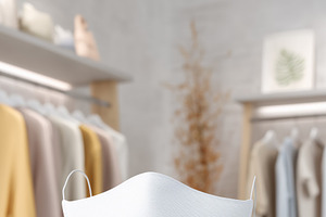 A white face mask mockup on a stand in a modern clothing store, with soft paste, a Mask Mockup by Textures & Backgrounds