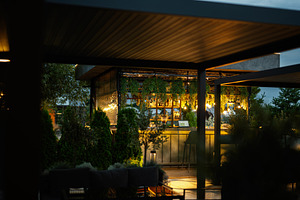 Outdoor rooftop bar with warm lighting surrounded by lush greenery at dusk, a Photo by AS photostudio