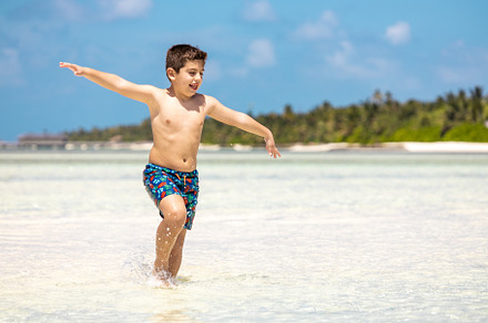 Funny kid running throw the water of a beach with open arms, a Person Photo by Cosca
