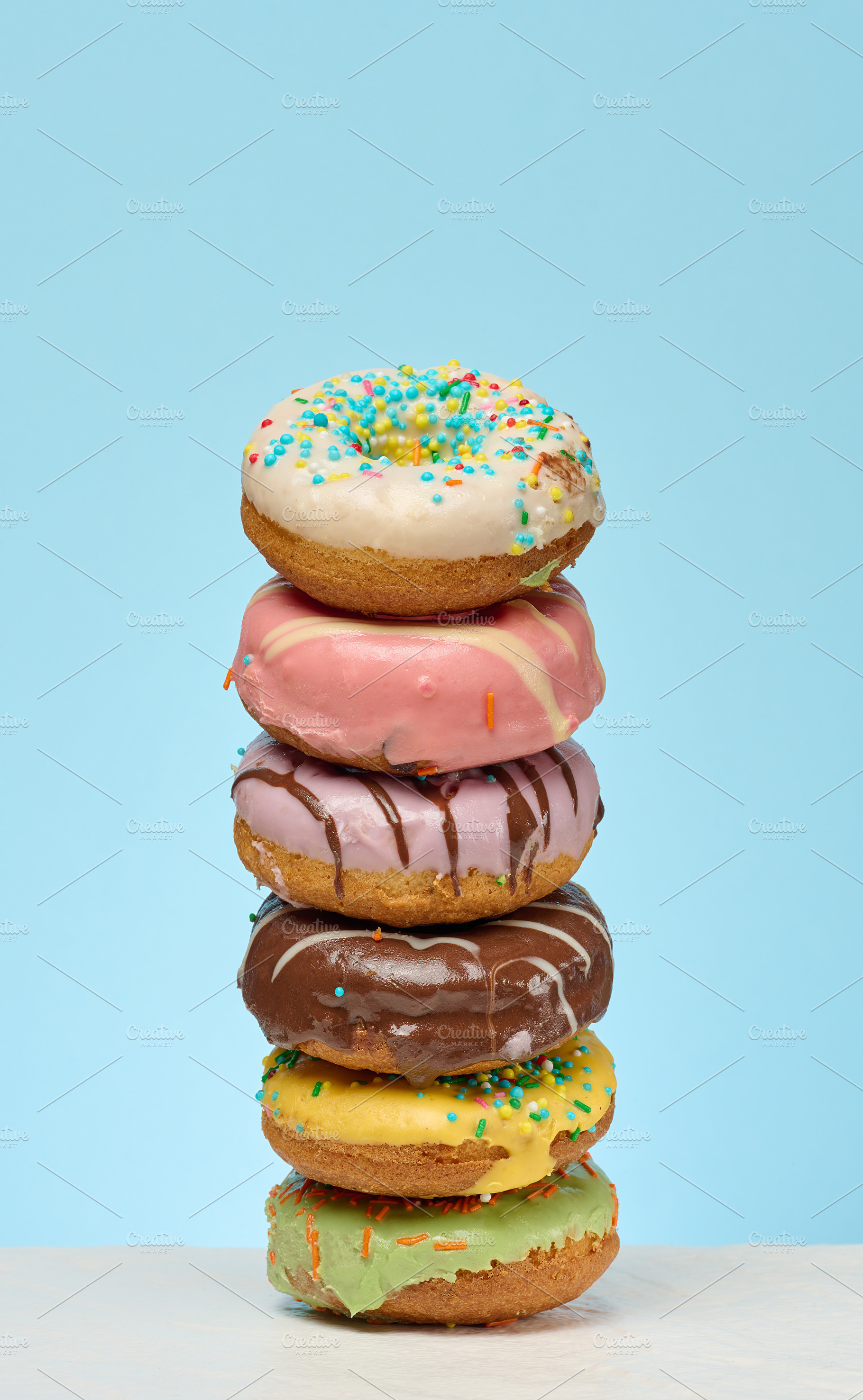 A tall stack of six colorful, glazed donuts with various topping, a Food & Drink Photo by ndanko
