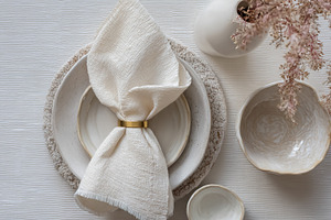 Dining table setting with a folded linen napkin and gold ring on, a Photo by Studio ANNA