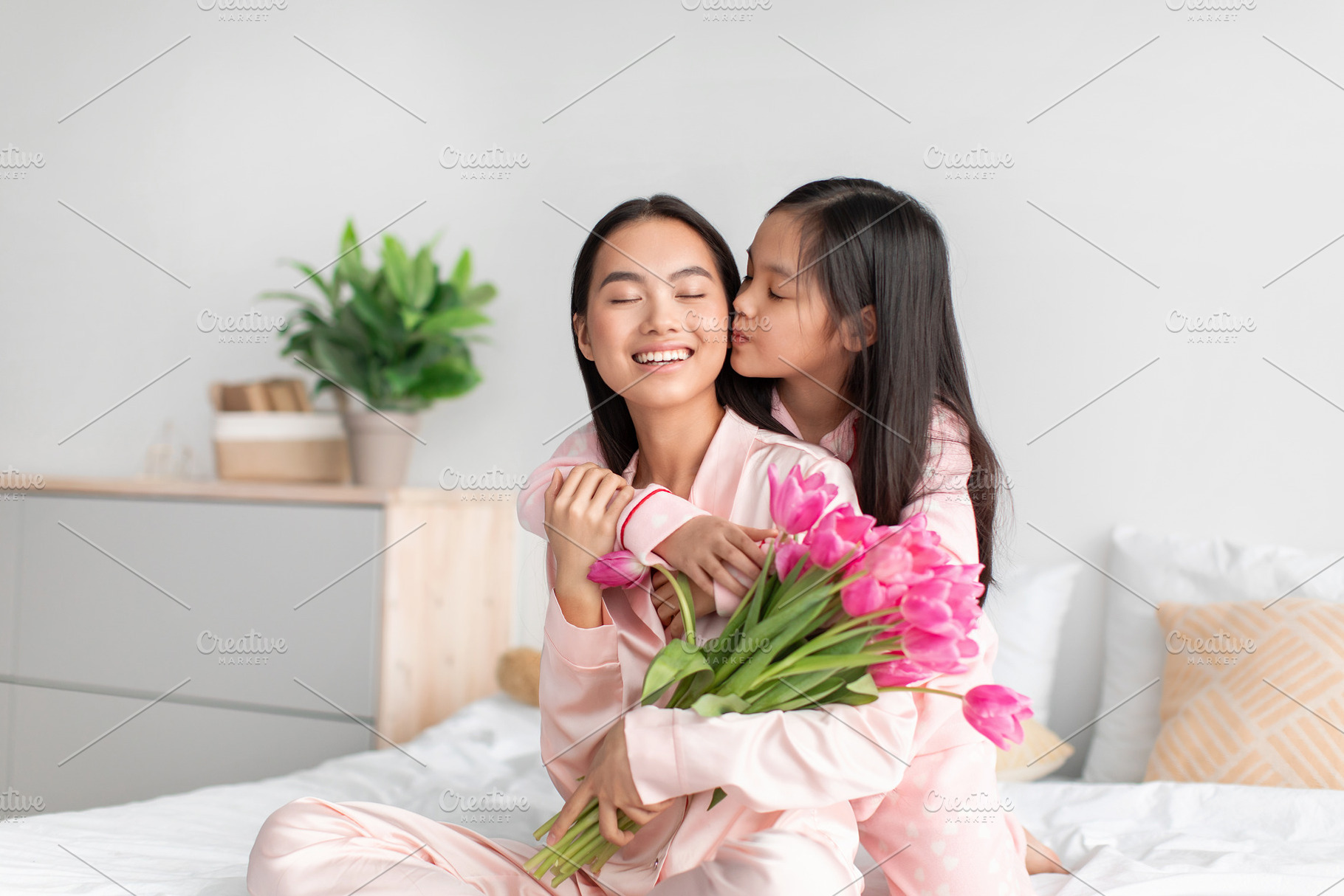 Smiling happy asian teenage girl kissing and hugging millennial woman with bouq, a Photo by Prostock-Studio