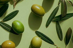 Green olives and olive leaves scattered on a light green backgro, a Photo by Studio ANNA