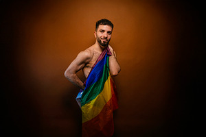 Young man proudly holding rainbow flag celebrating lgbtq+ pride, a Photo by karrastock