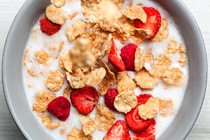 Cornflakes and freeze dried berries falling into a bowl of milk creating a heal, a Food & Drink Photo by Antonio Gravante Market