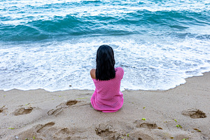 Young girl in pink dress sitting alone facing the ocean, waves gently rolling i, a Person Photo by Ales Munt