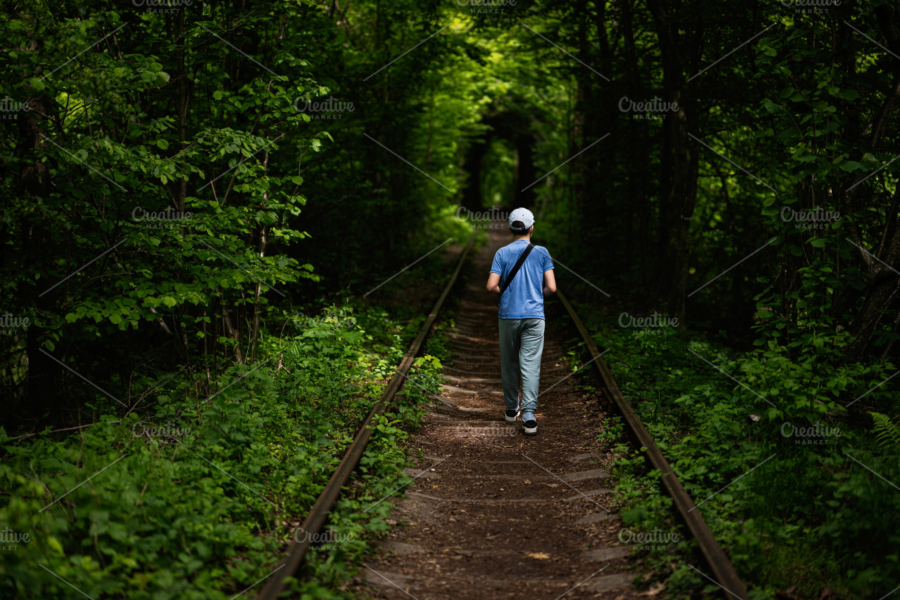 Boy walking along a scenic railway path surrounded by lush green foliage, a Photo by AS photostudio