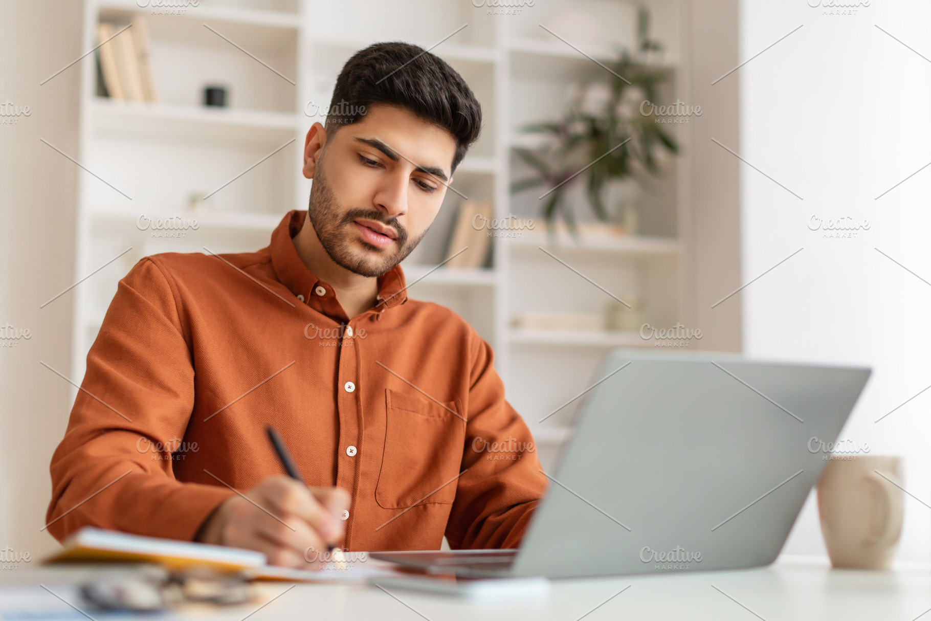 Portrait of focused Arab man using pc and writing, a Photo by Prostock-Studio