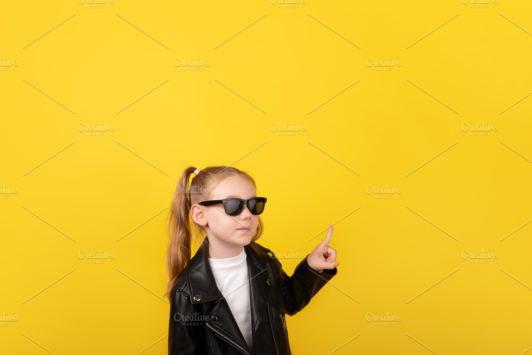 Young girl in black leather jacket and sunglasses pointing upwar, a Person Photo by Ales Munt