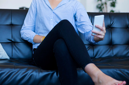 Barefoot brunette woman sitting on the sofa uses the mobile phone., a Person Photo by 2Design
