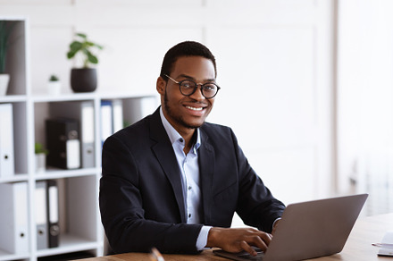 Cheerful african businessman working with laptop in office, a Photo by Prostock-Studio