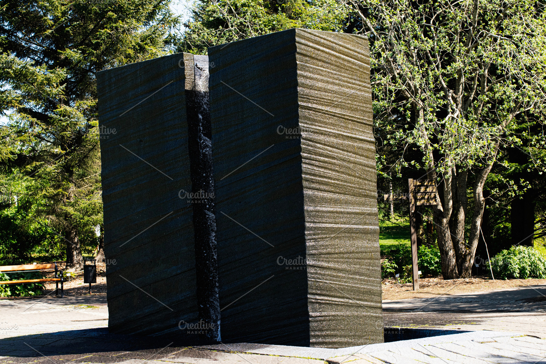 Outdoor basalt stone monument in serene park during sunny day with lush trees., a Photo by AS photostudio