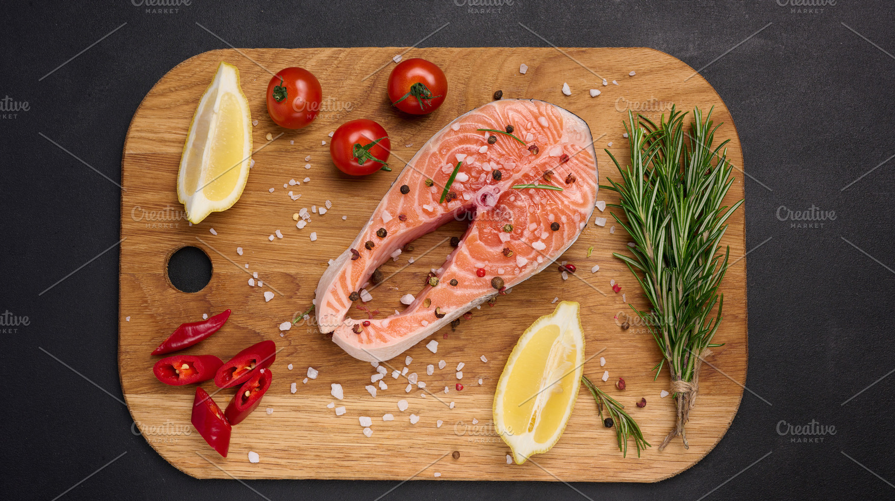 Raw salmon steak on a wooden cutting board, lemon slices, spices, a Food & Drink Photo by ndanko