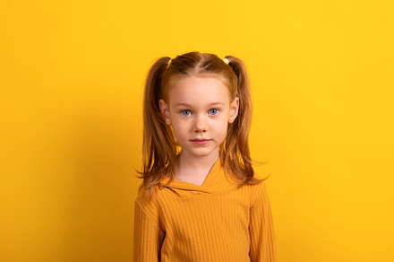 Young girl with pigtails wearing a mustard yellow sweater, stand