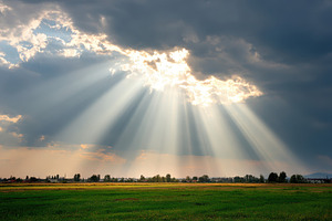 Sun rays through storm clouds over green field, a Nature Photo by AlyaAnd