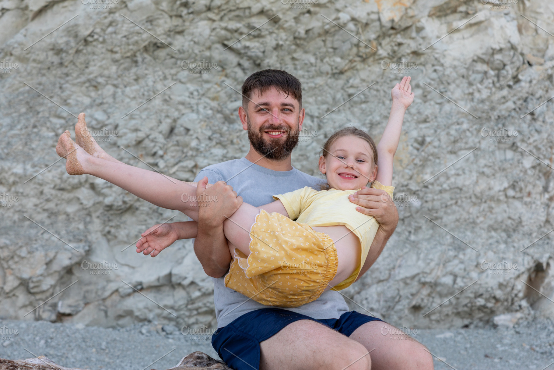Cheerful father holding his happy daughter against a rocky background, both smi, a Person Photo by Ales Munt