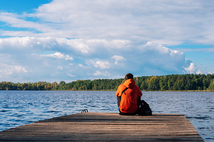A young man in a bright orange hoodie on a wooden pier against the background o, a Person Photo by PavelKant