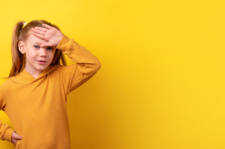 Young girl in a mustard sweater holding her hand to her forehead