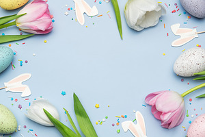 Easter eggs and tulips creating a frame on light blue background, a Photo by Olena Rudo
