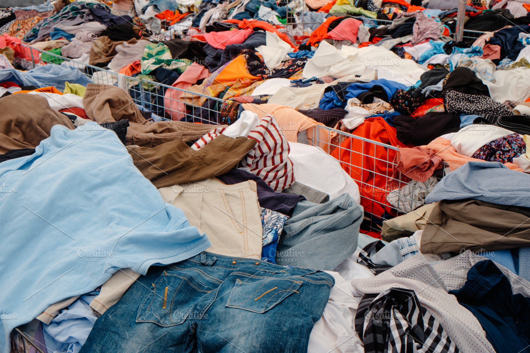 piles of clothes stacked in bins at an outdoor market, a Photo by Nito