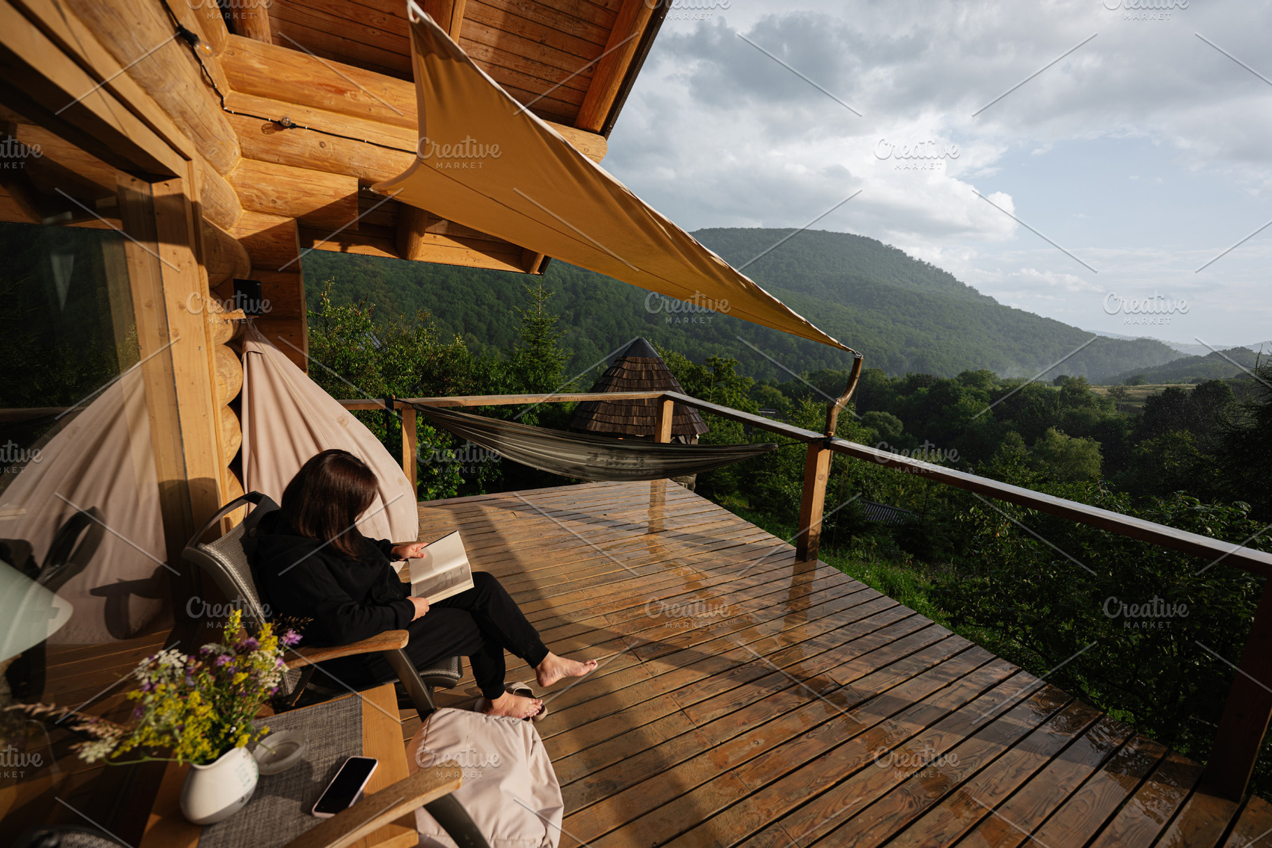 Woman reading on a cozy wooden terrace with scenic mountain views, a Photo by AS photostudio