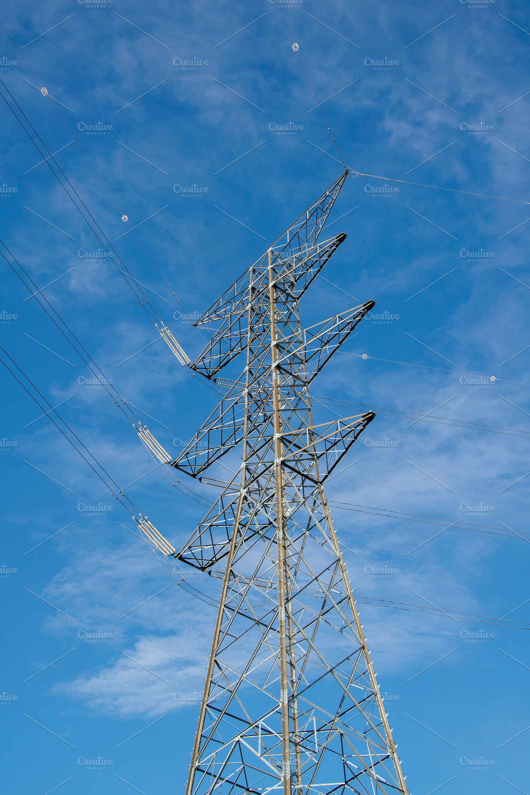 Low-angle view of an electrical tower against a blue sky, an Industrial Photo by DanFLCreativo