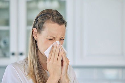 Closeup of sick caucasian woman holding tissue and blowing her nose while at home. Woman suffering from seasonal allergy or flu, a Photo by Peopleimages.com
