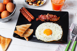 Delicious breakfast with fried egg, bacon, sausages and toasts on white wooden, a Food & Drink Photo by Antonio Gravante Market