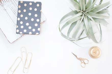 Minimalistic gold and white desk containing stock photo, gold paperclips, and