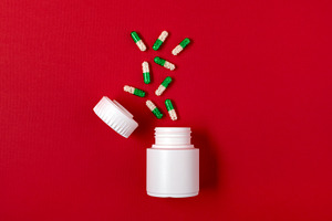 White plastic pill bottle with scattered green and white capsules on a vibrant, a Health & Medical Photo by Ales Munt
