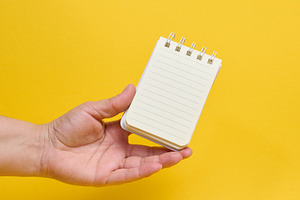 A person holding a small spiral-bound lined notepad on their pal