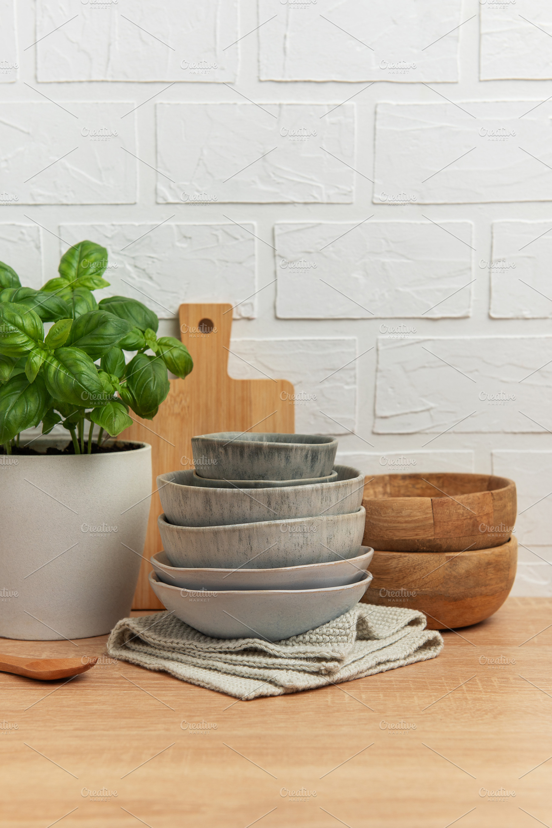 Kitchen table setting featuring stacked bowls, fresh basil, and, a Food & Drink Photo by Olena Rudo