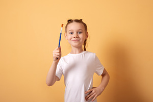 Cheerful young girl in a white t-shirt holding a paintbrush agai, a Person Photo by Ales Munt