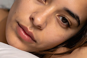Young woman lying on pillow with soft relaxed gaze, a Person Photo by GoodGoods