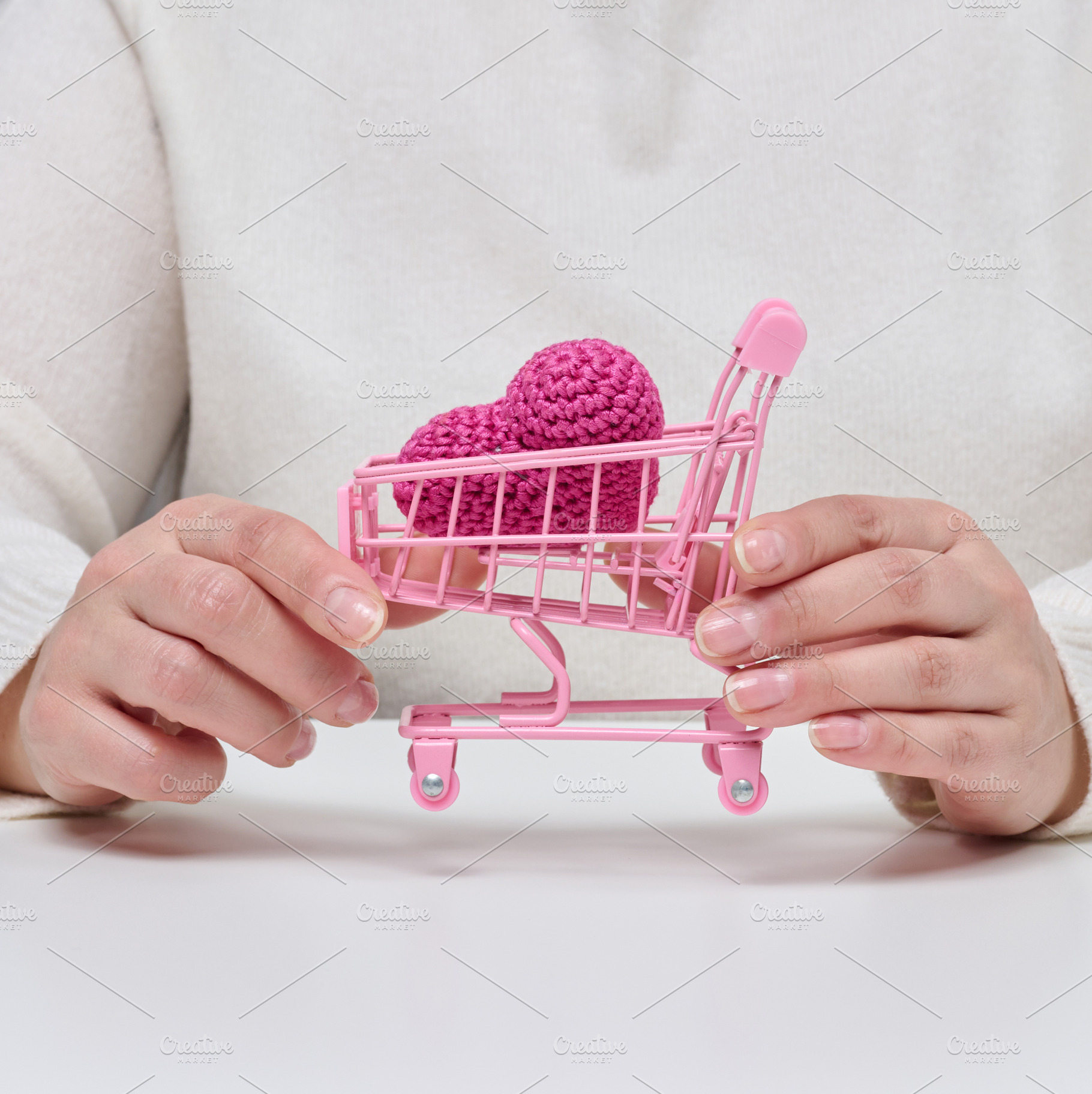 Female hands holding a small pink shopping cart with a knitted p, a Person Photo by ndanko