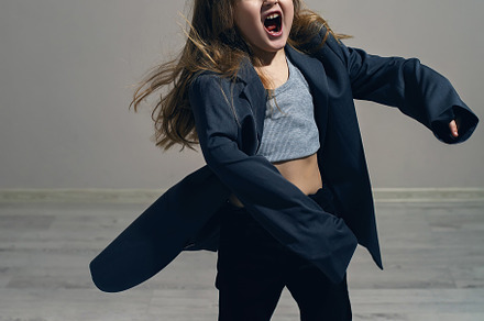 funny portrait of a fashionable girl child in a large gray jacket stands agains, a Person Photo by SaulichPhoto