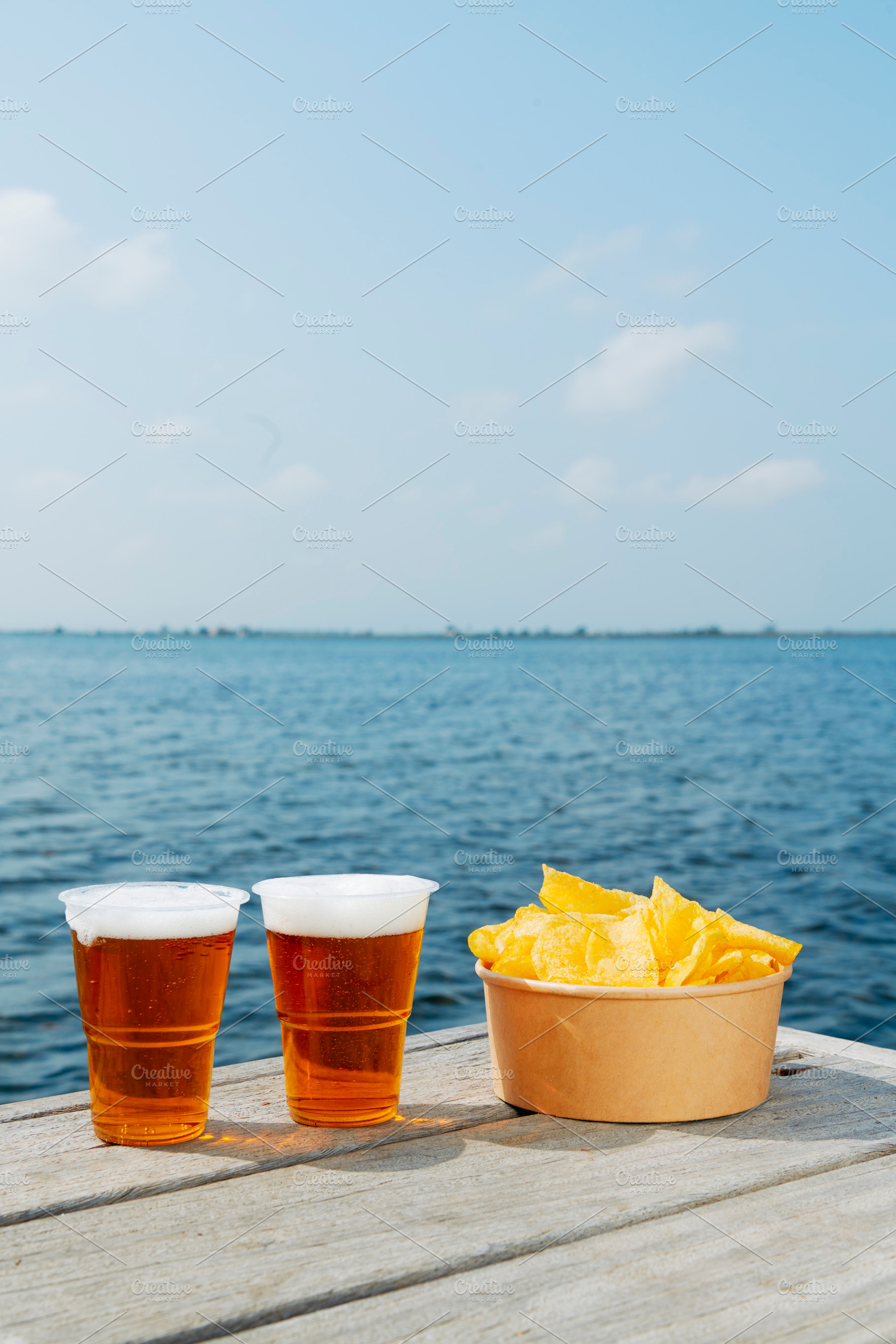 cups with beer and some potato chips on a dock, a Photo by Nito