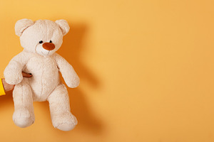 Hand holding a soft plush teddy bear against a vibrant orange ba, a Person Photo by Ales Munt