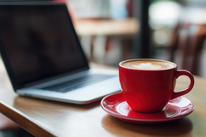 Red coffee cup sits beside a laptop, a Photo by Pavel_design