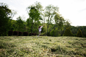 Child playing joyfully outside on a grassy field surrounded by lush trees, a Person Photo by AS photostudio