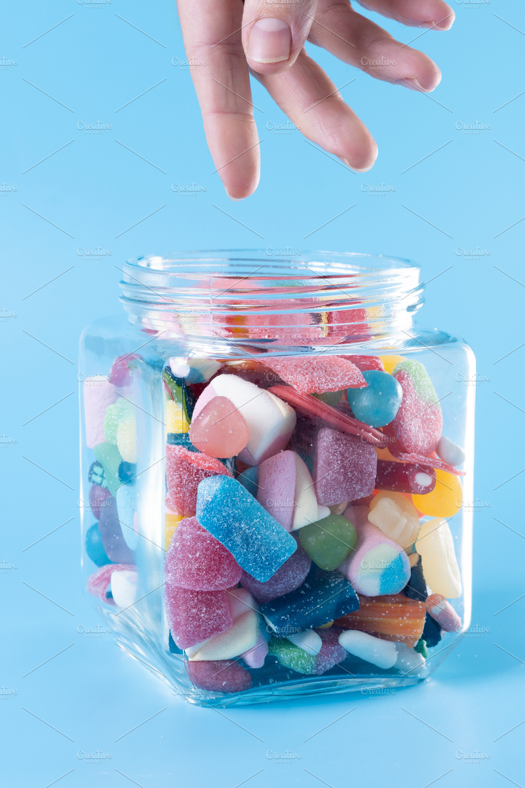 Hand reaching for colorful gummy candies in glass jar, a Food & Drink Photo by etorres69