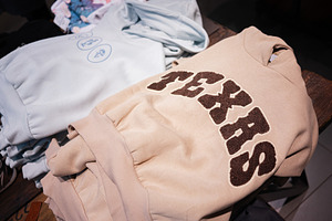 Stacked Beige and White Sweatshirts with Decorative Text Texas Design on Table, a Photo by AS photostudio